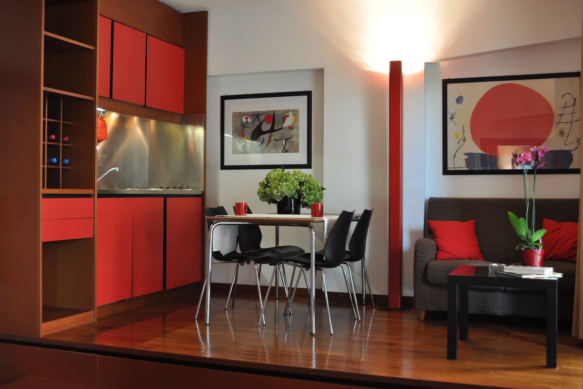 A modern living room with a dining area, red cabinets, a coffee table, and a sofa with red cushions.