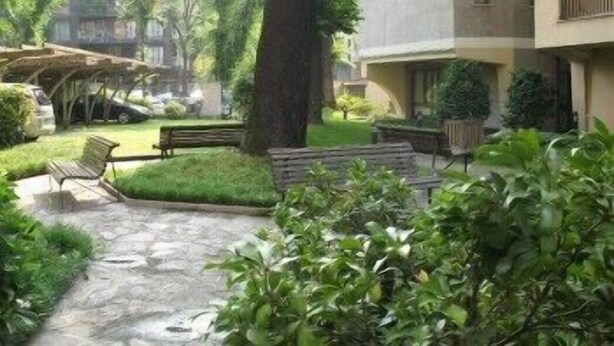 A courtyard with a stone pathway, benches, and greenery. - Residence Le Corti (Milan)