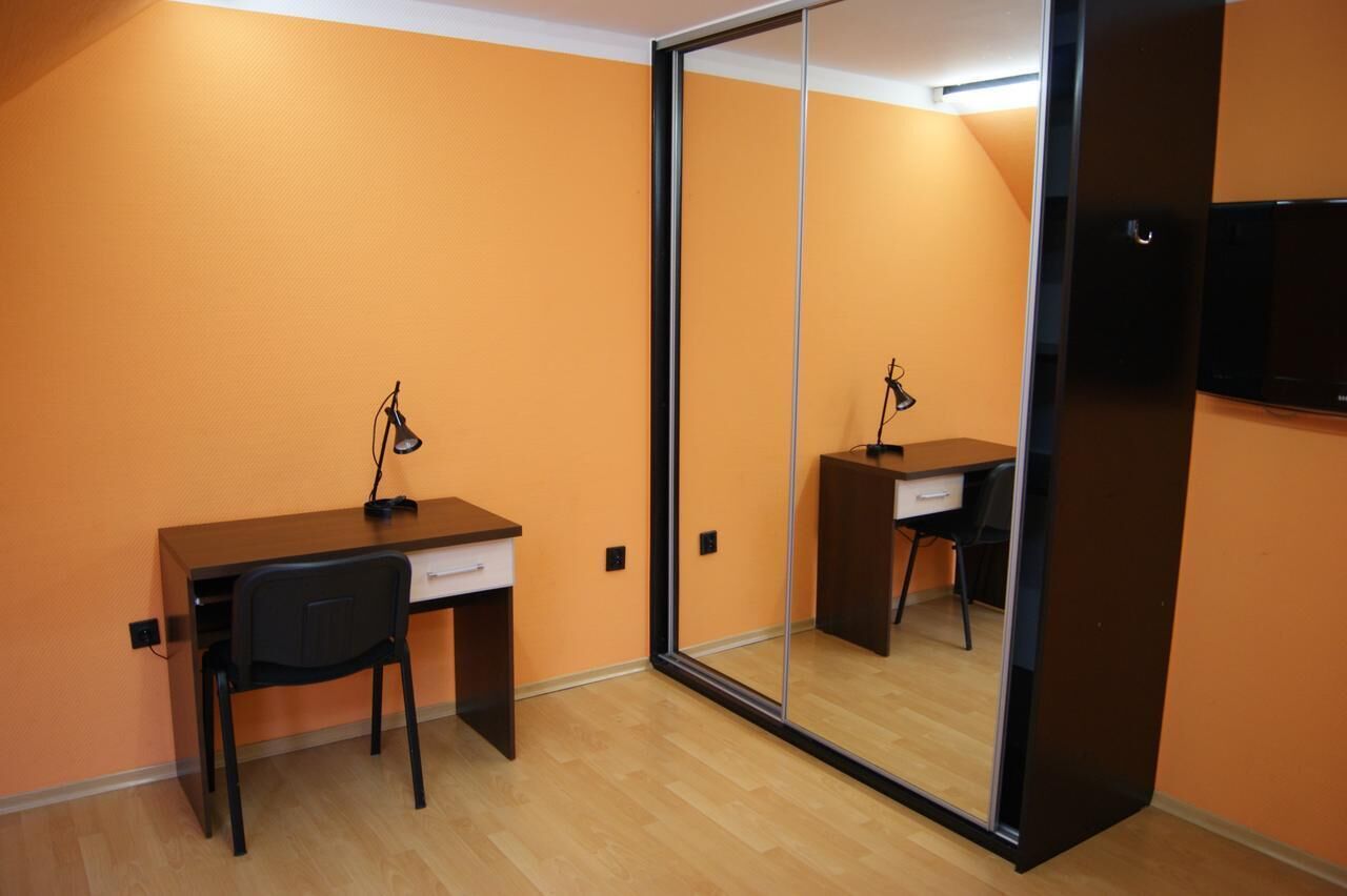 Una habitación con un escritorio de madera, una silla, un espejo y un televisor en la pared.