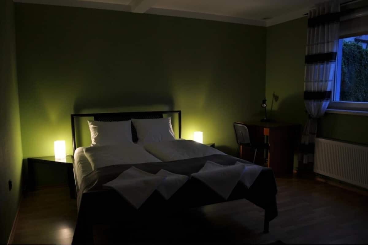 A bedroom with a bed, nightstands, a desk, and a window with curtains.