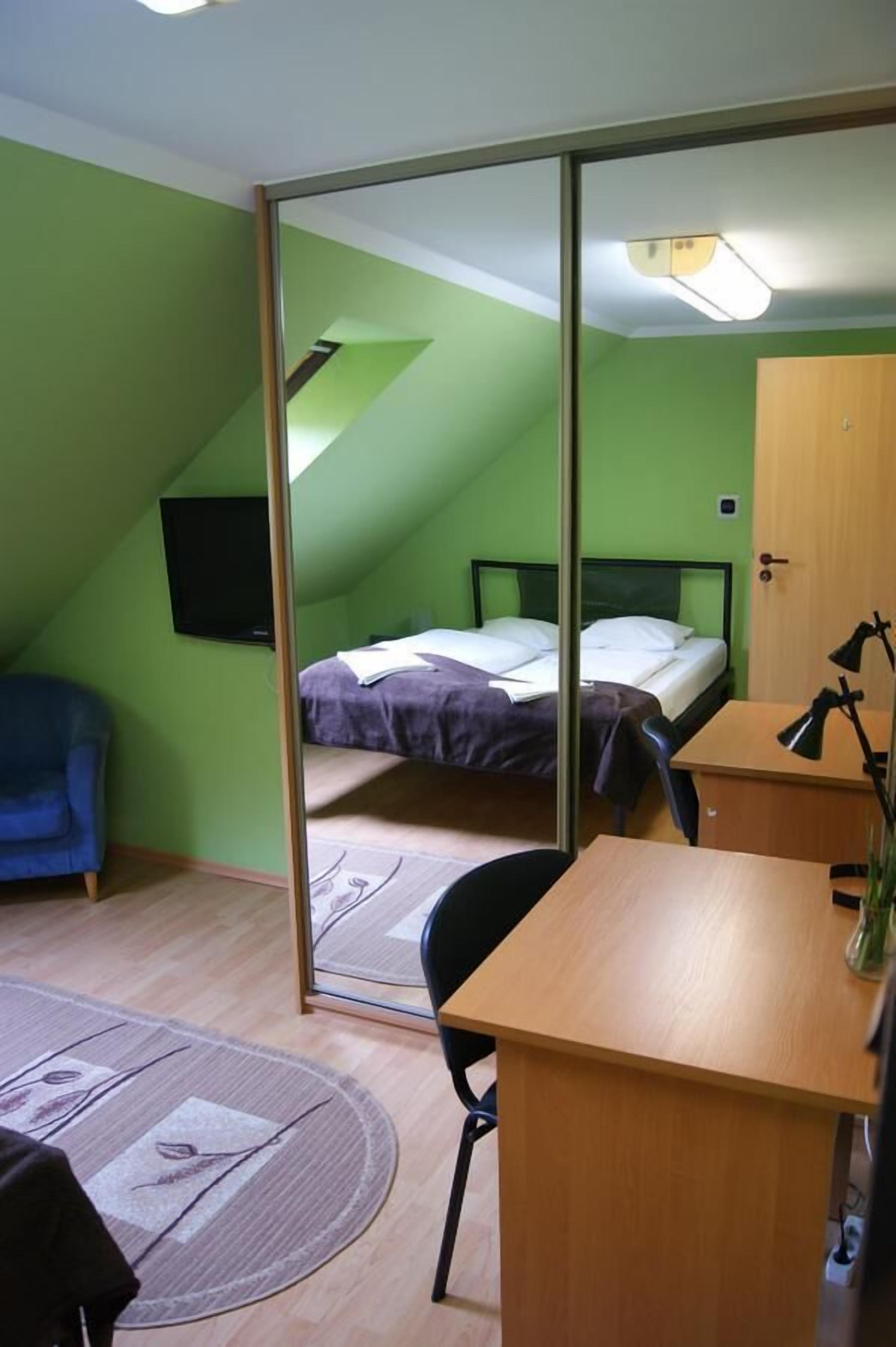 A small, green-walled room with a bed, a desk, and a chair.
