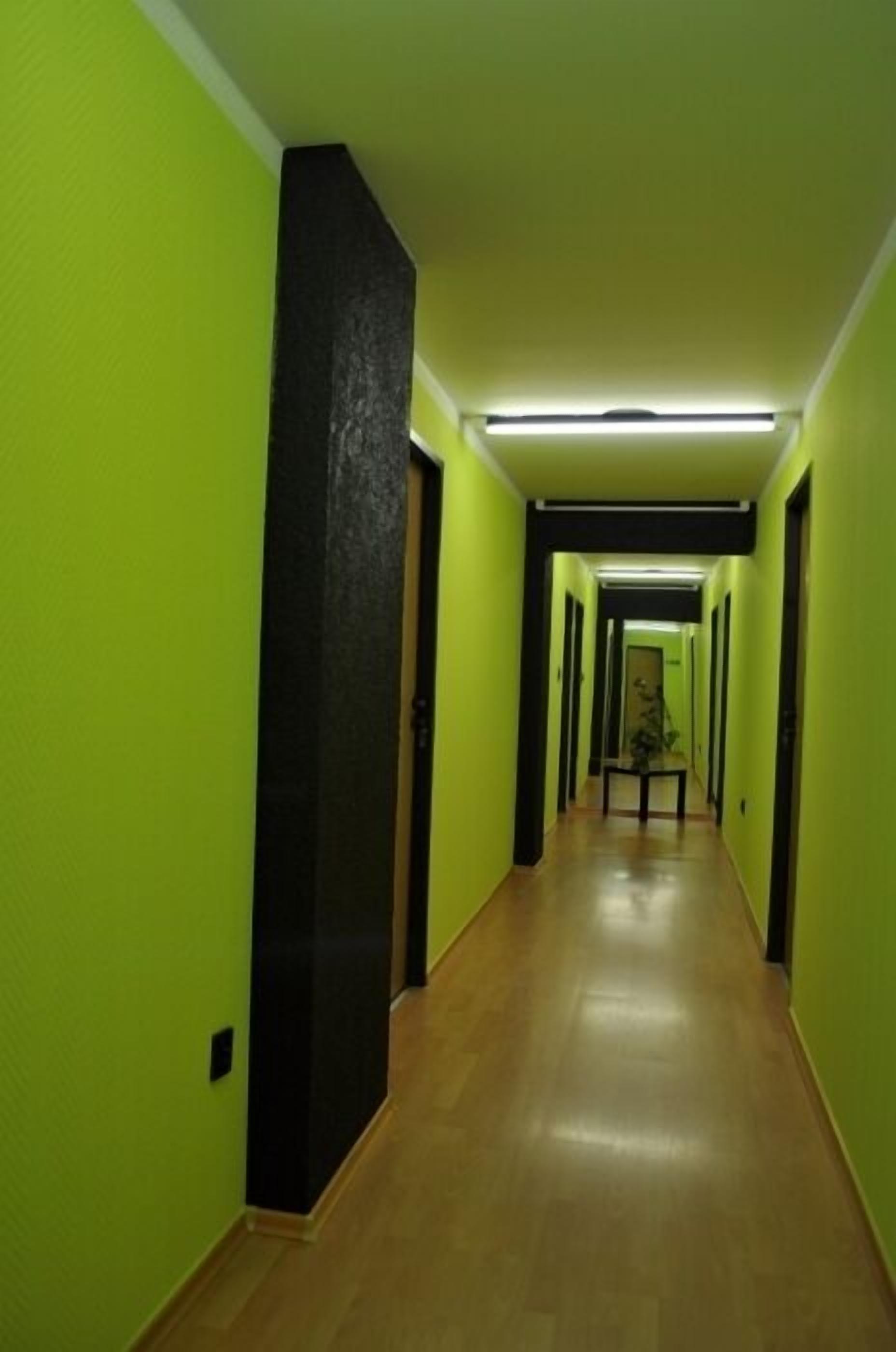 Un pasillo con paredes verdes y suelo de madera, que conduce a una puerta al final.
