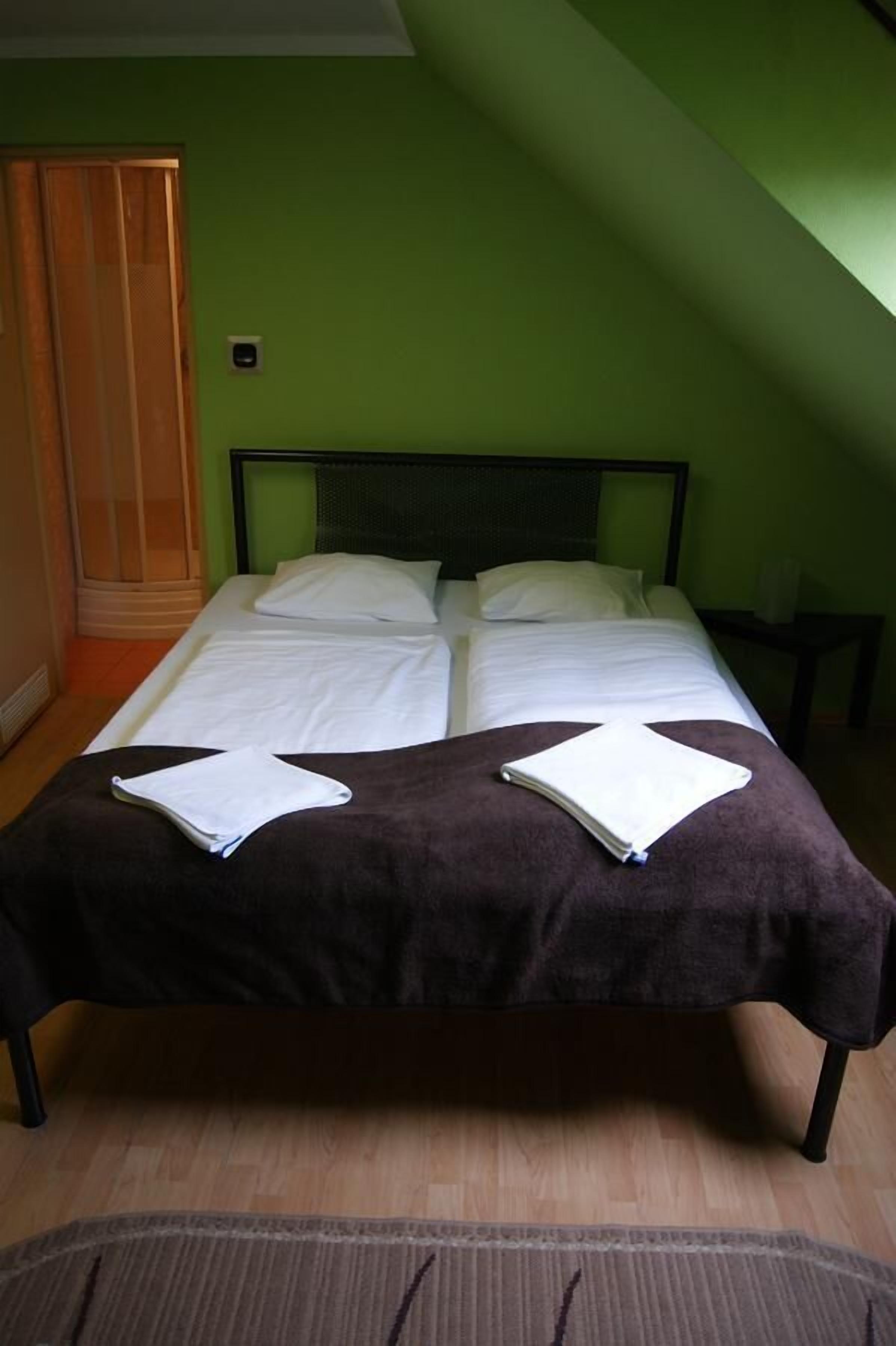 Een bed met witte lakens, een bruine deken en twee opgevouwen handdoeken.