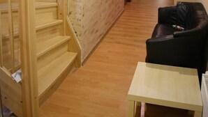 Een gang met houten vloeren, een trap, een zwarte leren bank en een kleine tafel.