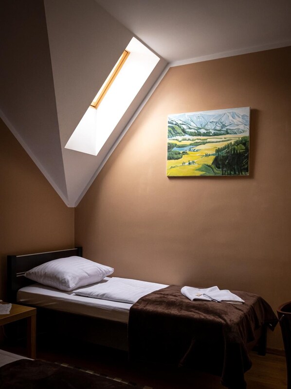 A bedroom with a skylight, a bed, a painting on the wall, and a small table.