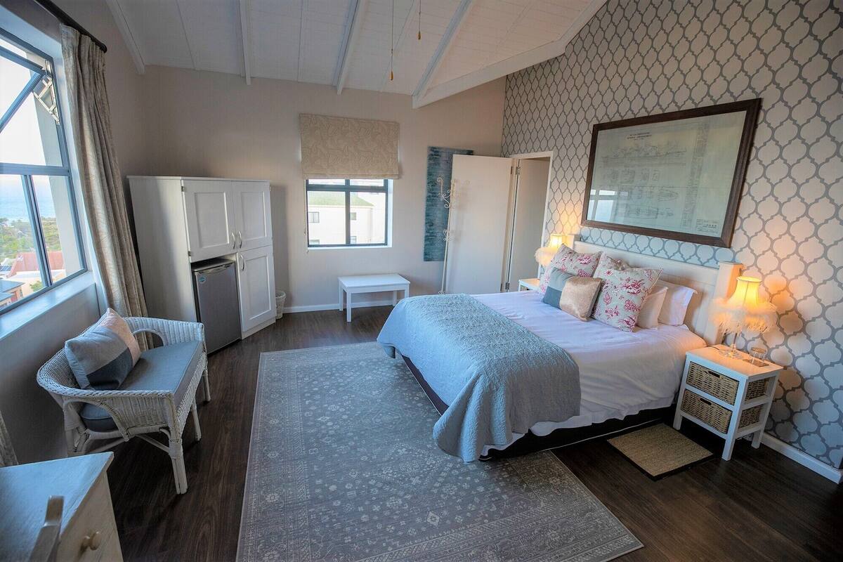 Quarto com cama, mesas de cabeceira, uma cadeira, guarda-roupa e janela com cortinas.