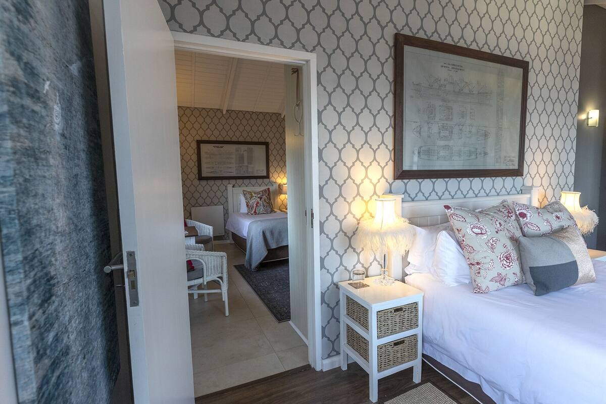 Quarto de hotel com cama, mesas de cabeceira e um desenho arquitetônico emoldurado na parede.