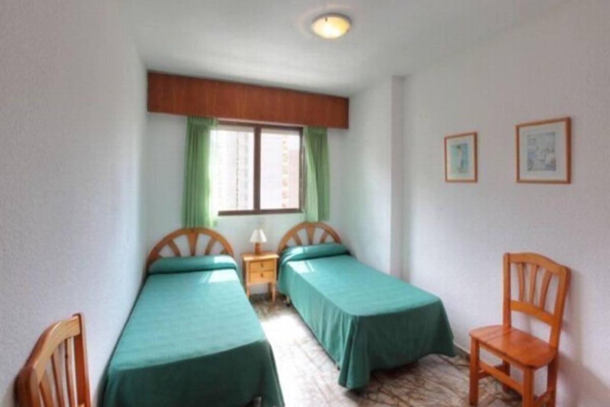 A small room with two single beds, a wooden chair, a nightstand, and a window with curtains.