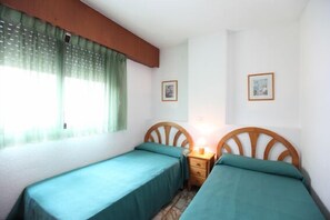 A room with two single beds, a wooden headboard, a bedside table with a lamp, and two framed pictures on the wall. - Apartamentos Carlos V (Benidorm)