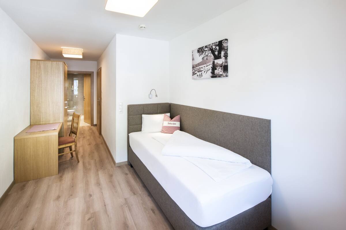 A compact hotel room with a single bed, a desk, and a chair.