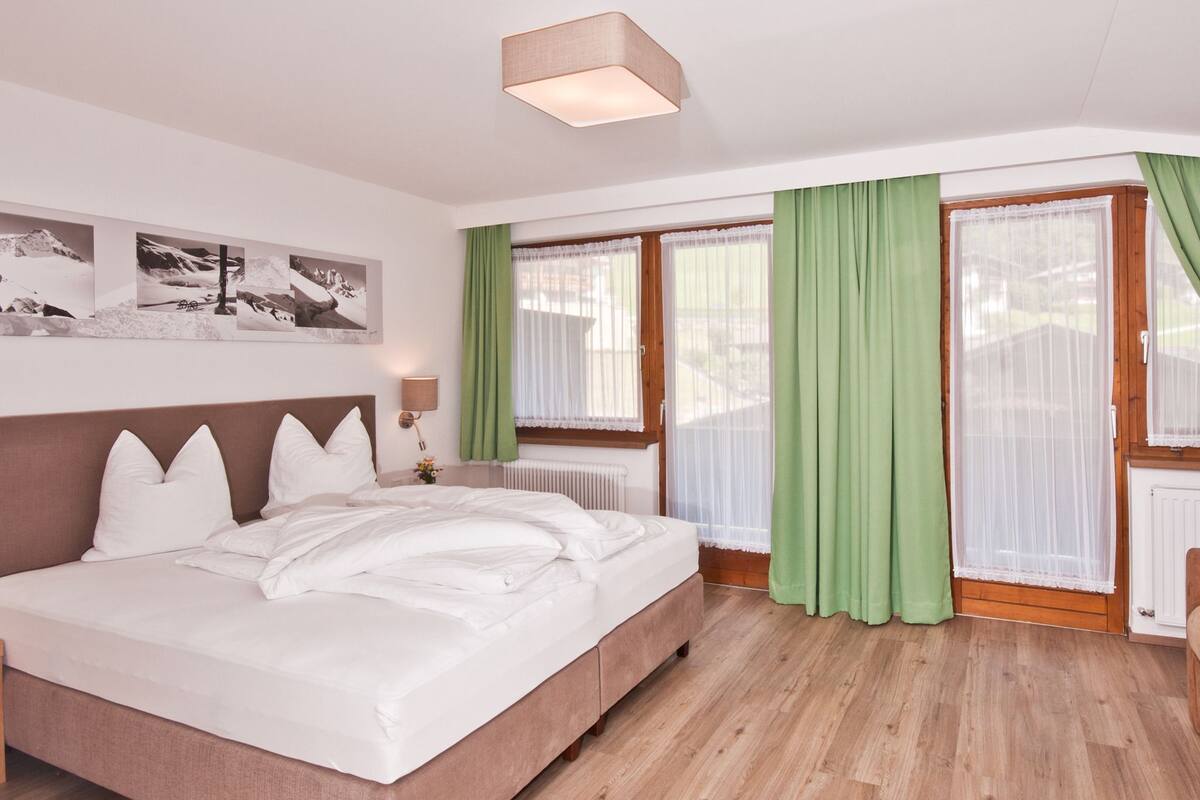 A bedroom with a large bed, wooden floor, green curtains, and a radiator.