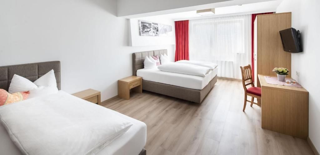 Habitación de hotel con dos camas, un escritorio, un televisor y una ventana con cortinas.