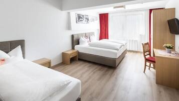 Habitación de hotel con dos camas, un escritorio, un televisor y una ventana con cortinas.