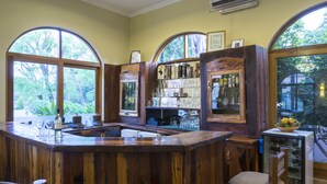 A rustic bar area with wooden furnishings, large arched windows, and a view of greenery outside.