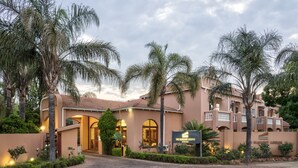 A hotel with a beige facade, arched entrance, and palm trees.
