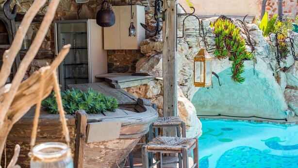 A rustic outdoor seating area with a stone wall, a wooden boat-shaped bench, and a small stool.