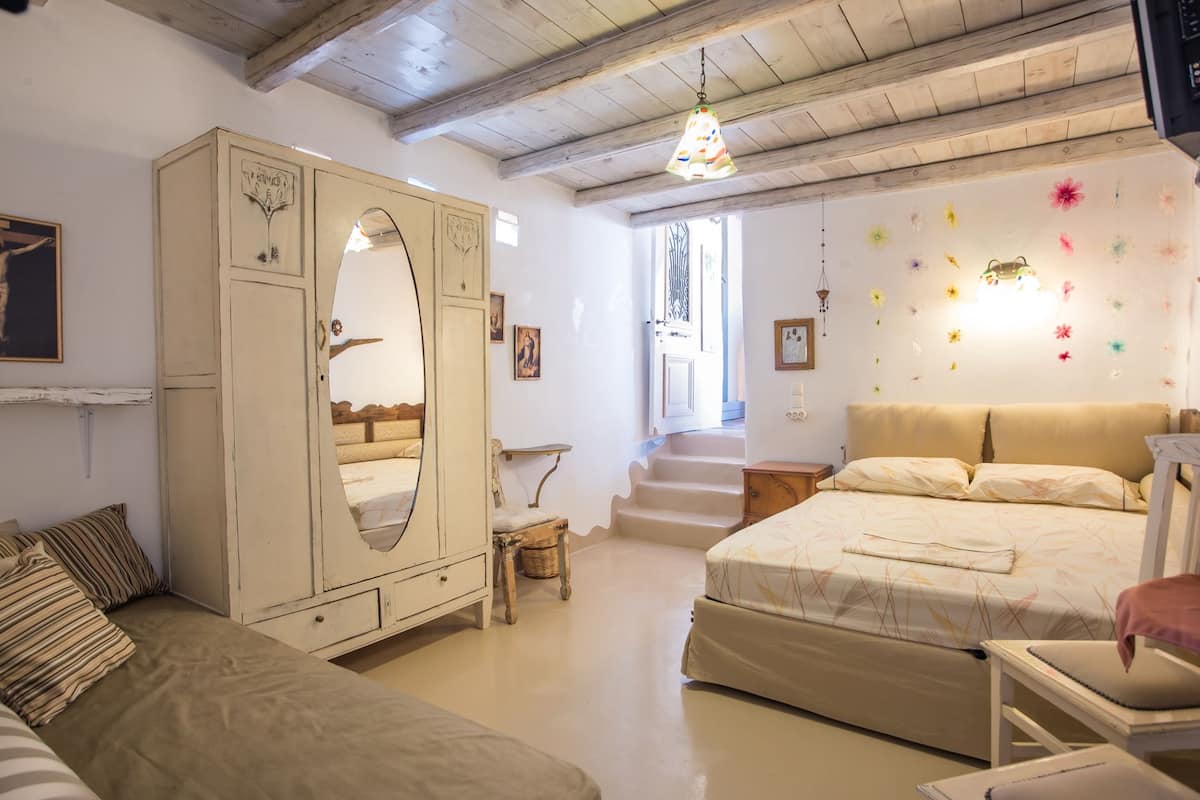 Un dormitorio con un armario grande, una cama con colcha estampada, una silla y una escalera que lleva a otra habitación.