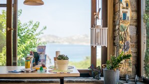 A table with various items including books, a candle, and a potted plant, set against a scenic view of the sea.