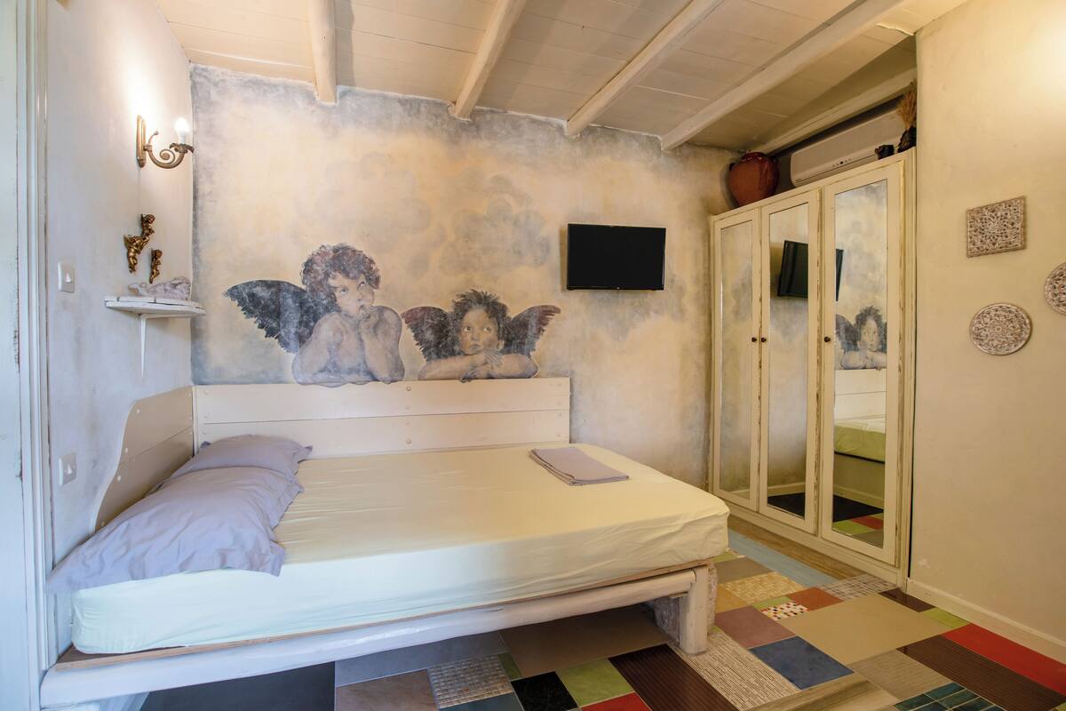 Un dormitorio con cama, televisor montado en la pared, espejo y techo con vigas a la vista.