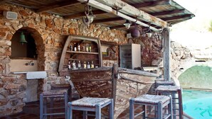 A rustic outdoor bar area with stone walls, wooden bar counter, and stools.
