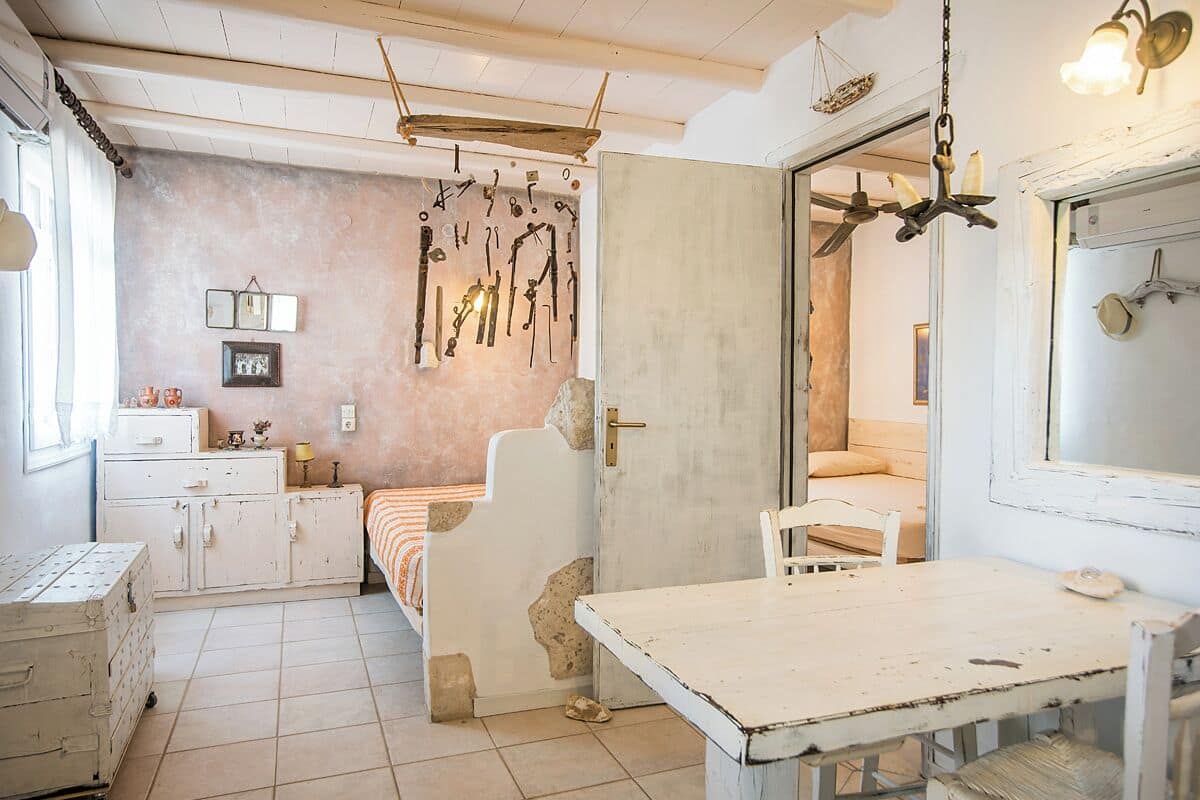 Una habitación de estilo rústico, con un armario blanco, una cama con colcha anaranjada y blanca a rayas, una mesa de madera y una pared decorada con utensilios de cocina colgantes.