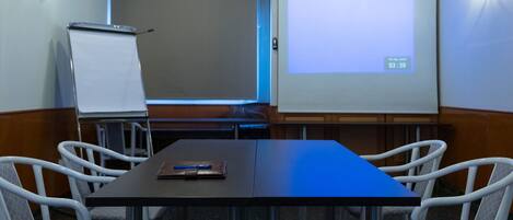 A conference room with a long table, four chairs, a whiteboard, and a projector screen displaying a timer.