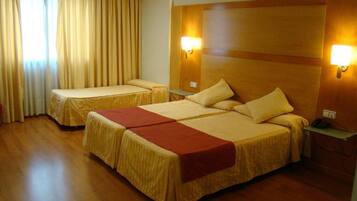 Een hotelkamer met twee bedden, een houten hoofdbord, bedlampjes en een raam met gordijnen.