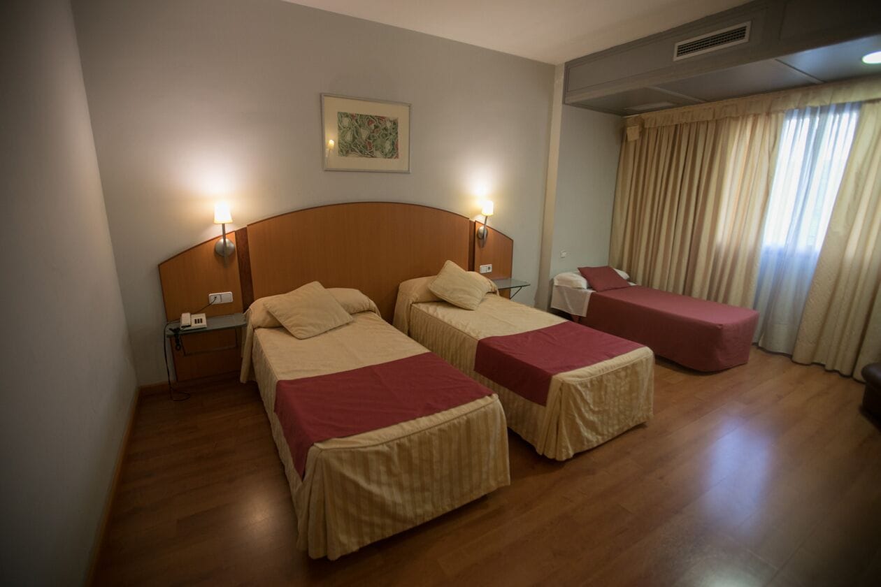 Een hotelkamer met twee bedden, een klein tafeltje en een raam met gordijnen.