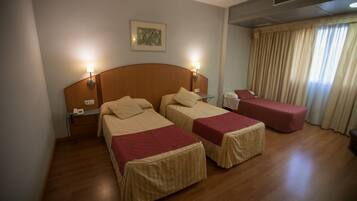 Een hotelkamer met twee bedden, een klein tafeltje en een raam met gordijnen.