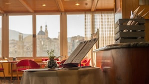A restaurant with a table set for two, a menu stand, and a view of a cityscape through large windows. - Hotel Reconquista (Alcoy)