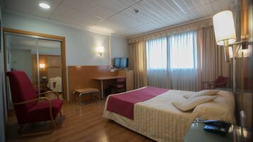 Una habitación de hotel con cama, escritorio, silla, televisor y lámpara.