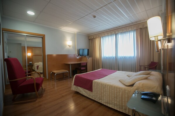 Una habitación de hotel con cama, escritorio, silla, televisor y lámpara.