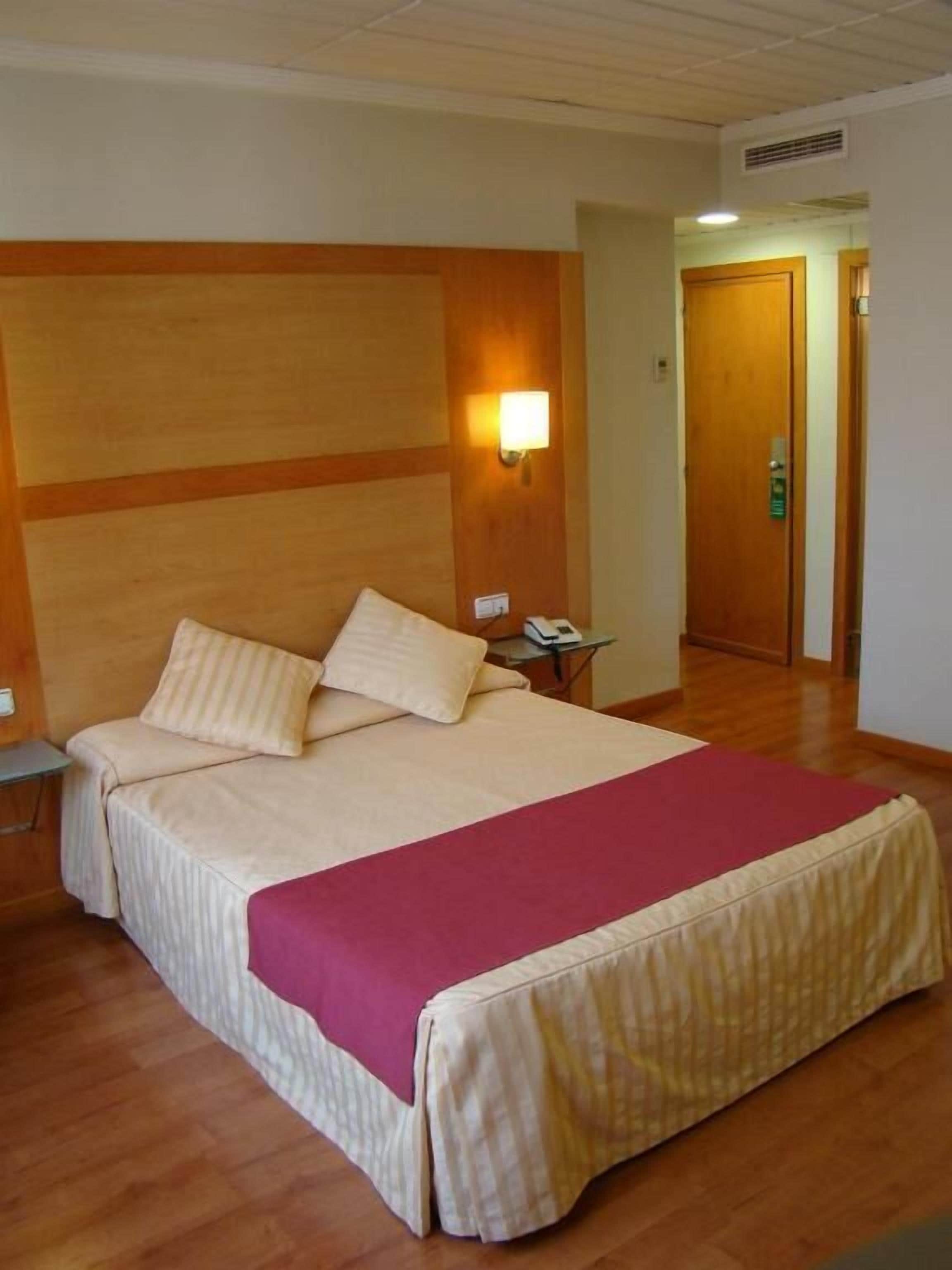 Habitación de hotel con una cama grande, una mesita de noche, una lámpara de pared y una puerta de madera.