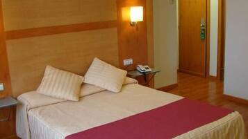 Habitación de hotel con una cama grande, una mesita de noche, una lámpara de pared y una puerta de madera.