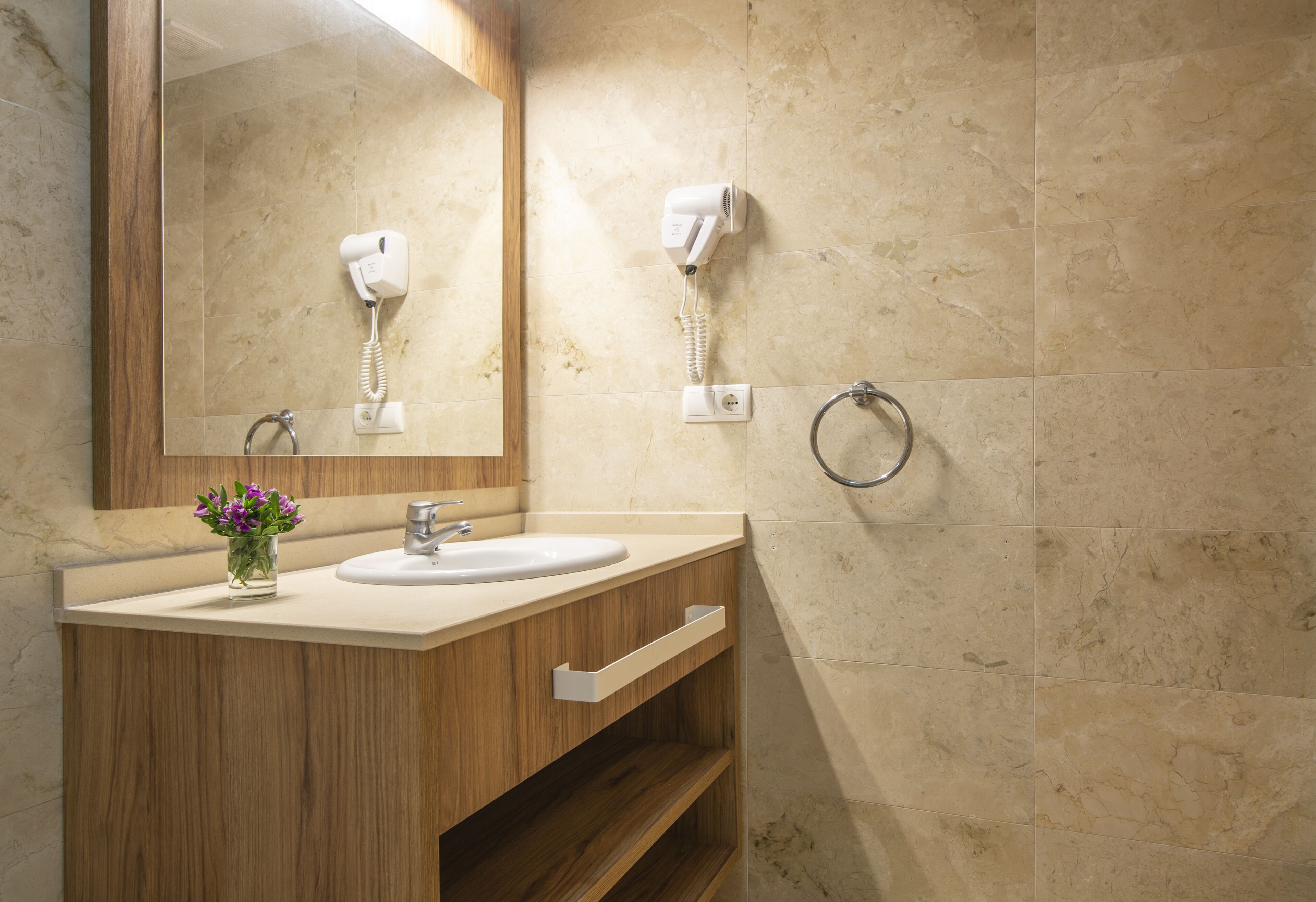 Un baño con tocador de madera, dos lavamanos, un espejo, un secador de pelo y un aro para toallas.