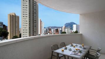 Un balcone con un tavolo apparecchiato per la colazione, con vista su un paesaggio urbano caratterizzato da alti edifici e montagne.