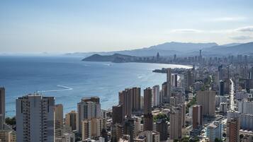 Un paisaje costero con edificios altos, una vista despejada del mar y montañas a lo lejos.