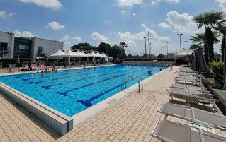 Una piscina con bordo piastrellato, poltrone a sdraio e ombrelloni.