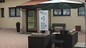 An outdoor seating area with wicker furniture and a green umbrella, a sign for 'Green Garden Resort', and a brick wall with windows. - Green Garden Resort (Mestre)