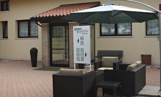 Un'area esterna con sedute in vimini, un ombrello verde, un cartello con la scritta 'Green Garden Resort' e un muro in mattoni con finestre.