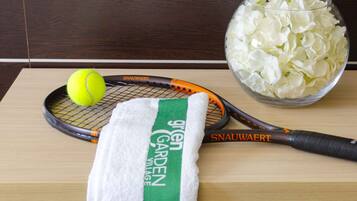 A tennis racket, a tennis ball, and a bowl of white flowers on a wooden table.