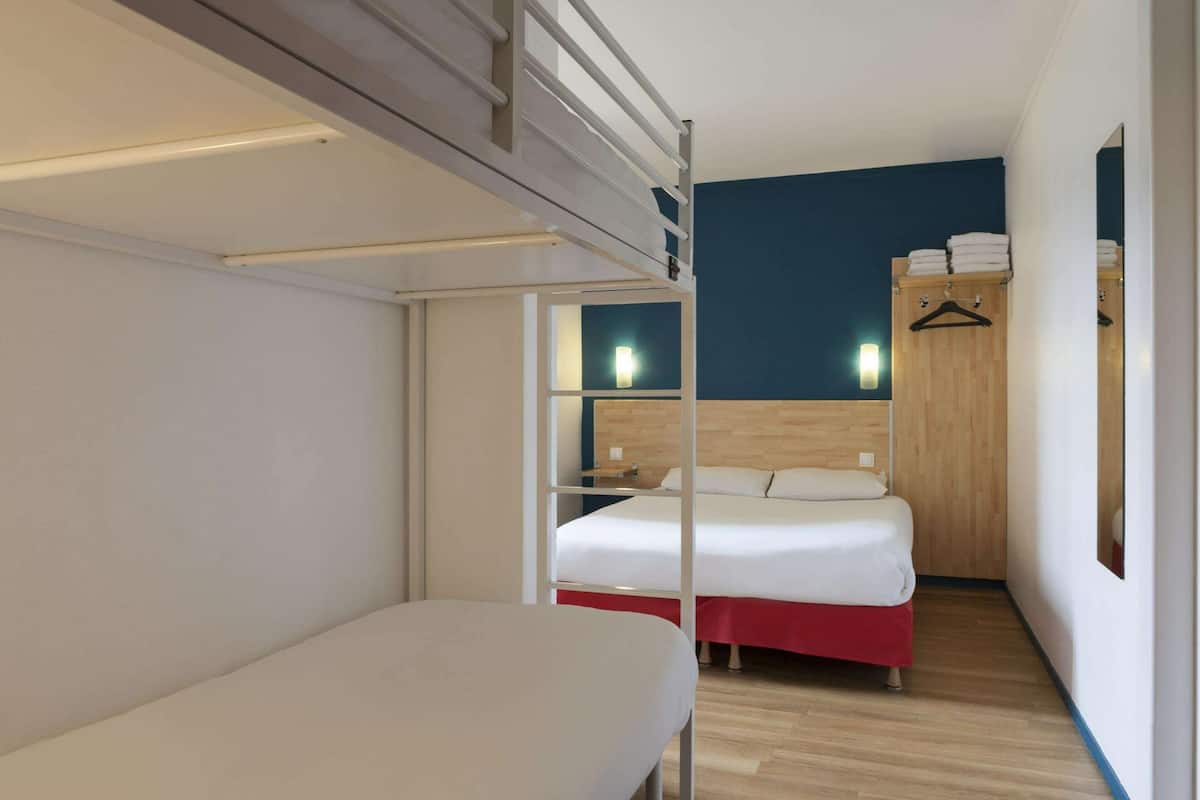 Ein Hotelzimmer mit Etagenbett, einem Einzelbett, einem Holzschrank und einem Spiegel.