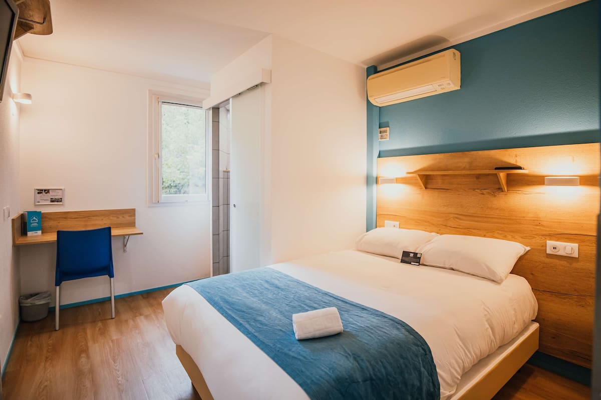 Ein Hotelzimmer mit Bett, Schreibtisch, Stuhl und Klimaanlage.