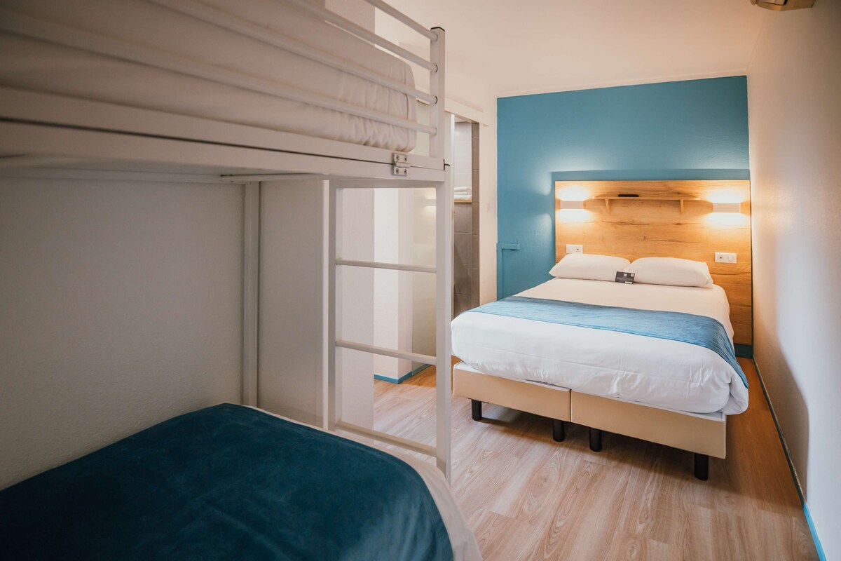Un dormitorio con una litera, una cama individual y un cabecero de madera con iluminación integrada.