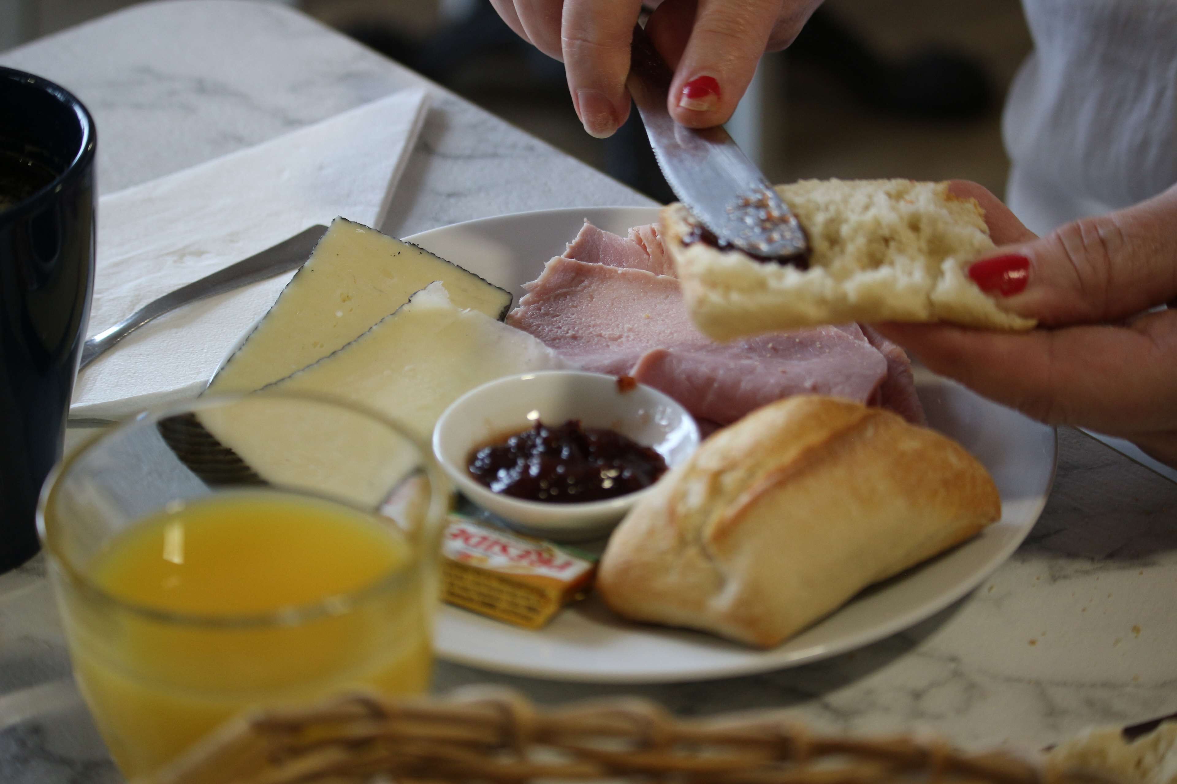 A plate with cheese, ham, a pastry, and a glass of juice.