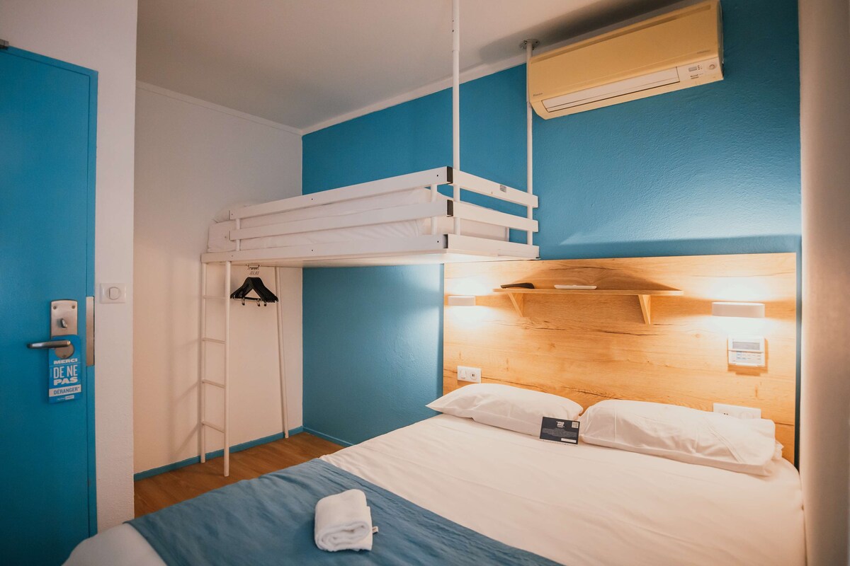 Habitación con literas, cabecera de madera, pared azul y una puerta con un letrero.