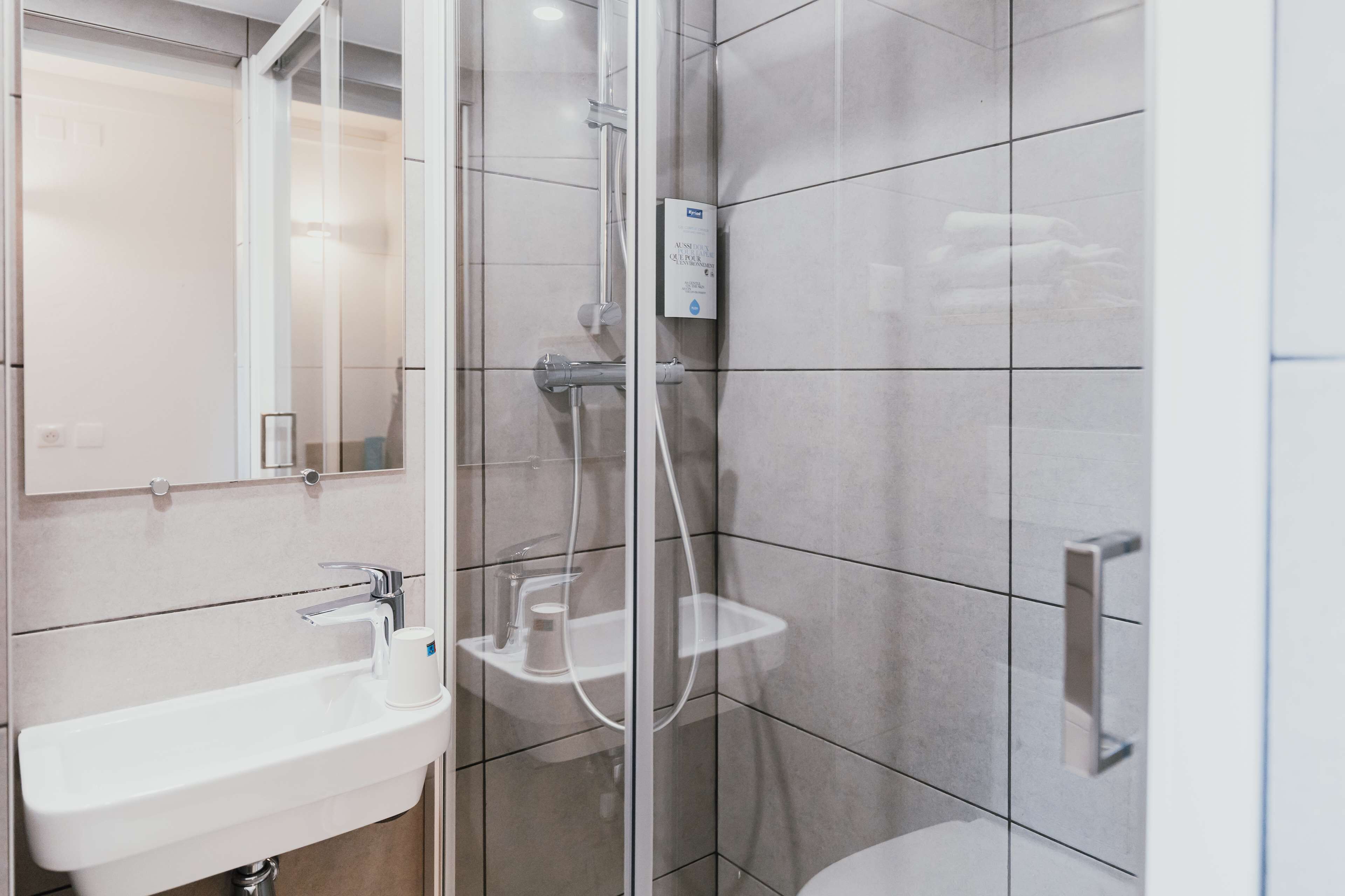 Ein modernes Badezimmer mit einer begehbaren Glasdusche, einem Waschbecken mit Spiegel und einer Toilette.