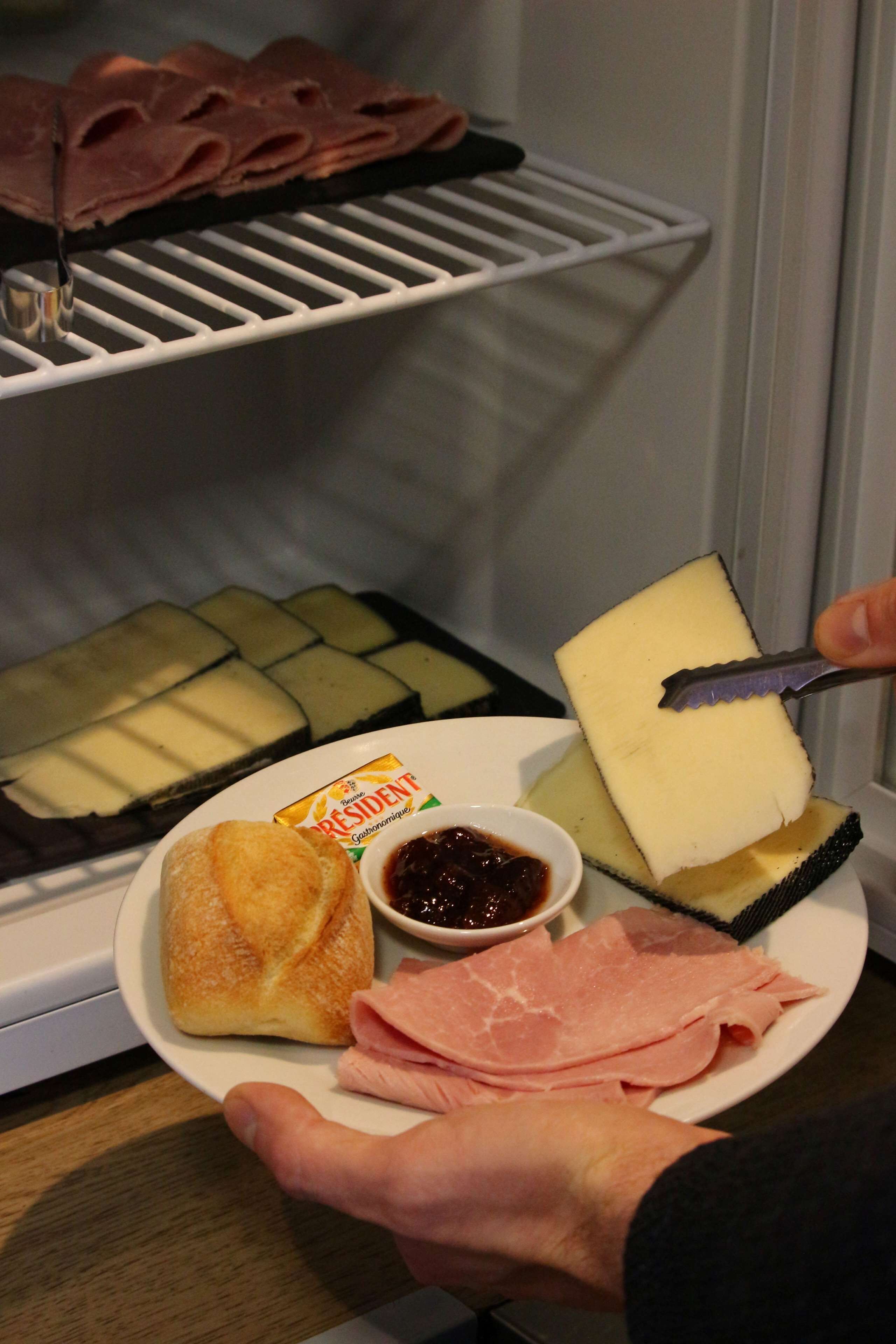 A plate with cheese, ham, a pastry, and a small bowl of jam.
