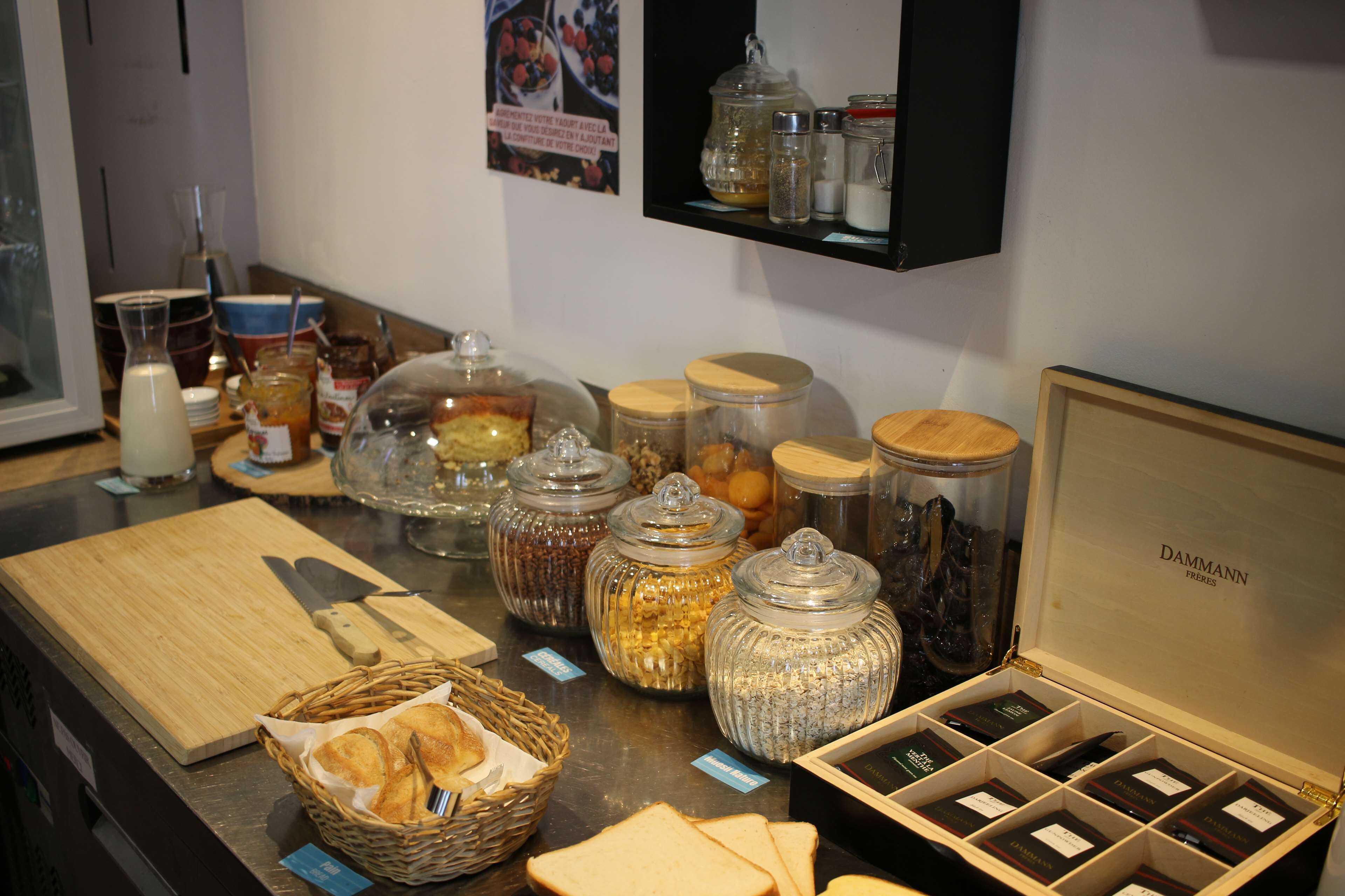 A buffet setup with various food items, including jars of condiments, a basket of bread, and a cutting board.