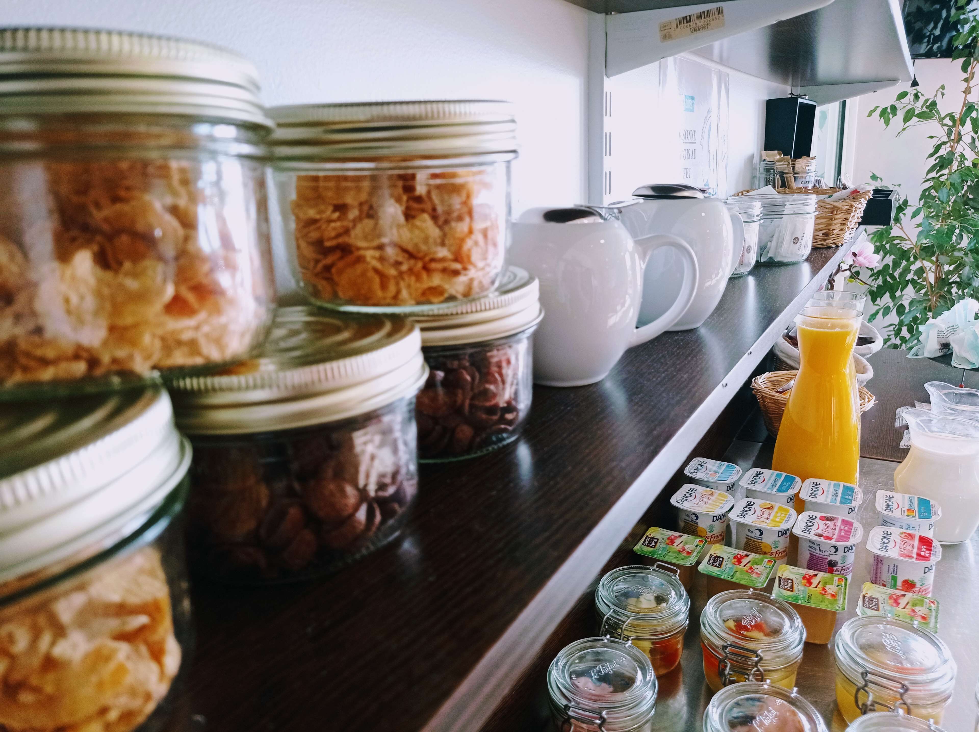 A breakfast bar with various food items and beverages, including jars of granola, coffee, and juice, as well as a selection of yogurt containers.